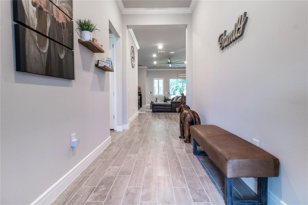 A hallway with wood-look tile flooring leads to a living area with a brown bench — 3414 MICHIGAN STREET, LAKE MARY, FL