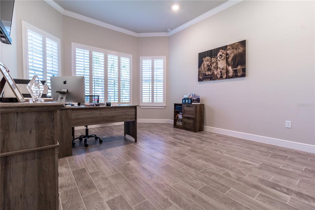 A home office features wood-look tile flooring, a desk with a computer, and plantation shutters — 3414 MICHIGAN STREET, LAKE MARY, FL