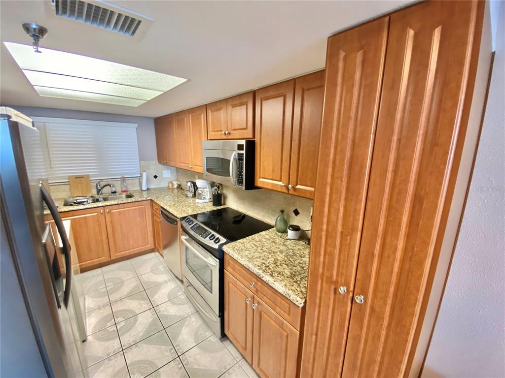 A kitchen features wood cabinets, granite countertops, stainless steel appliances, and tiled flooring — 6009 SEA RANCH DRIVE UNIT 507, HUDSON, FL