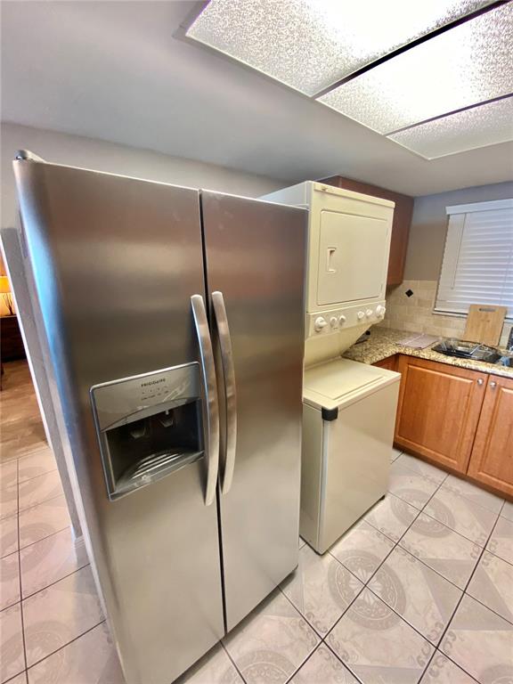 A kitchen features a stainless steel refrigerator next to a stacked washer and dryer unit — 6009 SEA RANCH DRIVE UNIT 507, HUDSON, FL