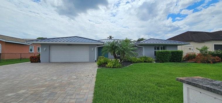 A single-story house with a metal roof, a paved driveway, and a manicured front lawn — 2871 CORAL WAY, PUNTA GORDA, FL