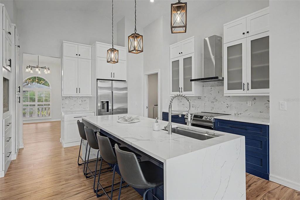 A kitchen features white upper cabinets, blue lower cabinets, a marble island, and pendant lights — 2815 89TH AVENUE E, PARRISH, FL