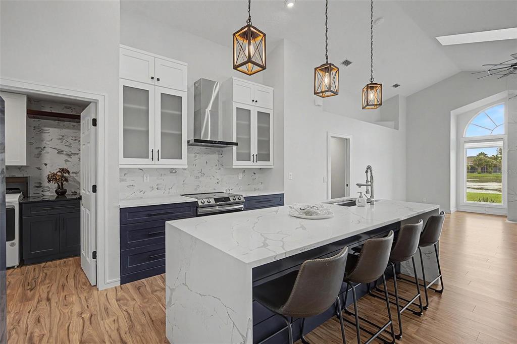 A kitchen features a large marble-topped island, dark blue cabinets, and three hanging pendant lights — 2815 89TH AVENUE E, PARRISH, FL