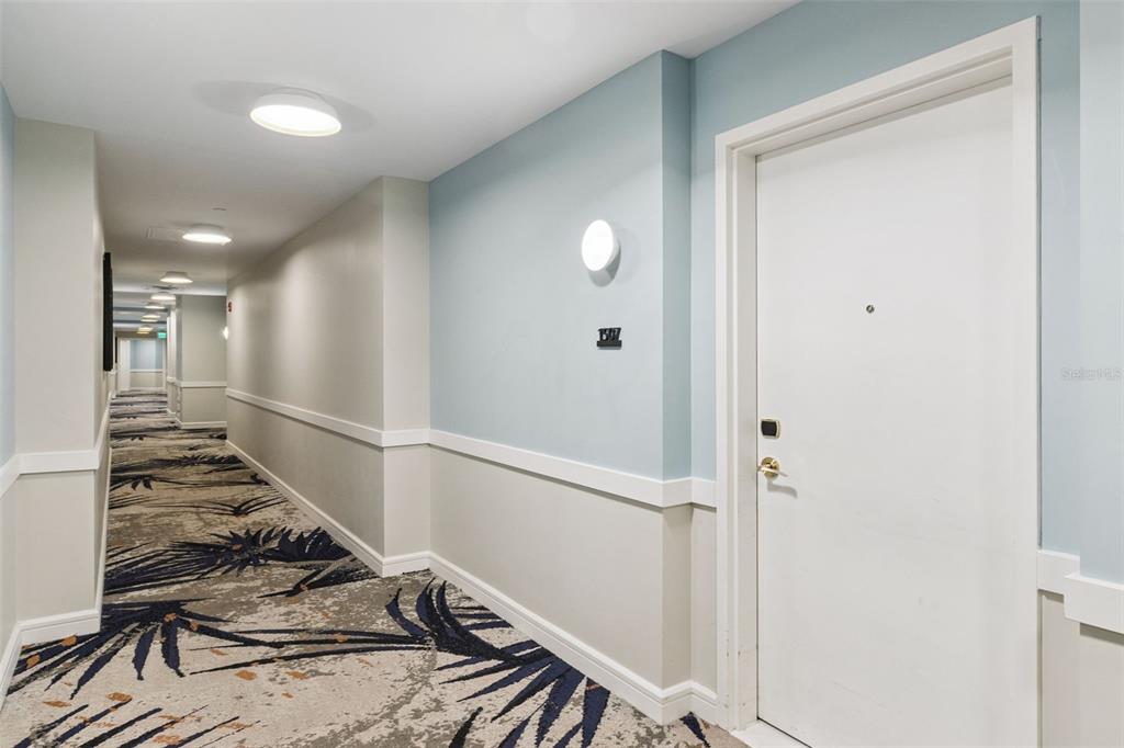 A long hotel hallway features patterned carpeting, light blue and beige walls, and a white door — 3151 SUNSET WALK DRIVE UNIT 1507, KISSIMMEE, FL