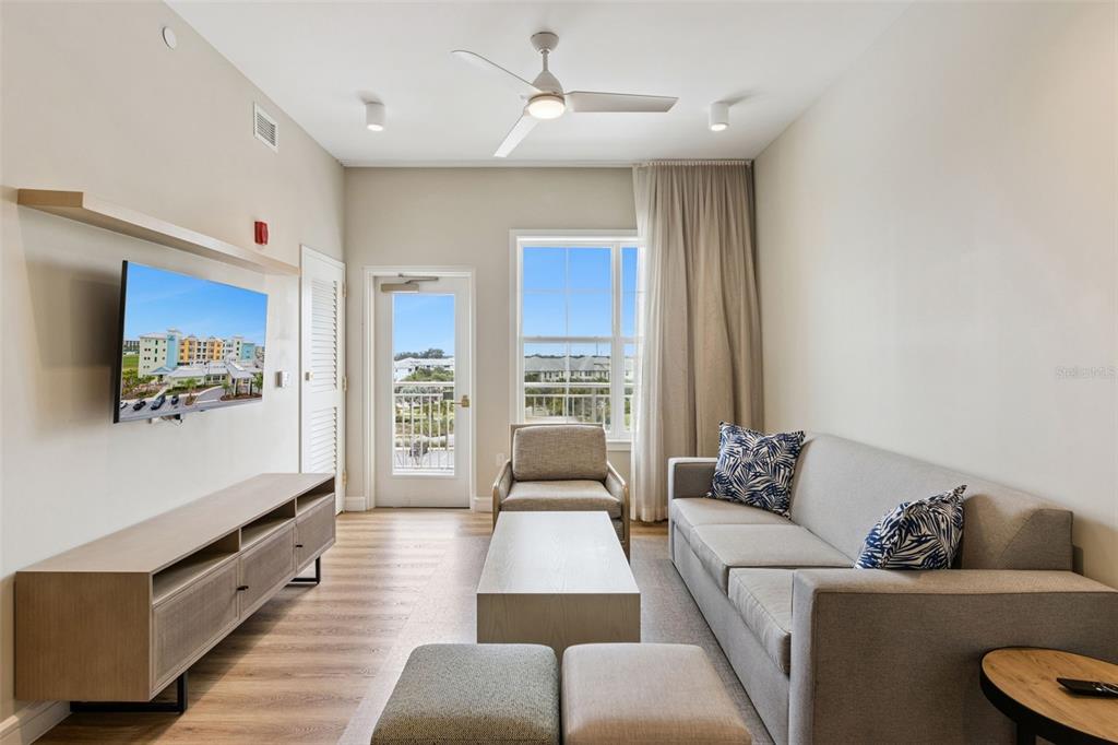 A living room features a sofa, armchairs, television, and a door leading to a balcony — 3151 SUNSET WALK DRIVE UNIT 1507, KISSIMMEE, FL