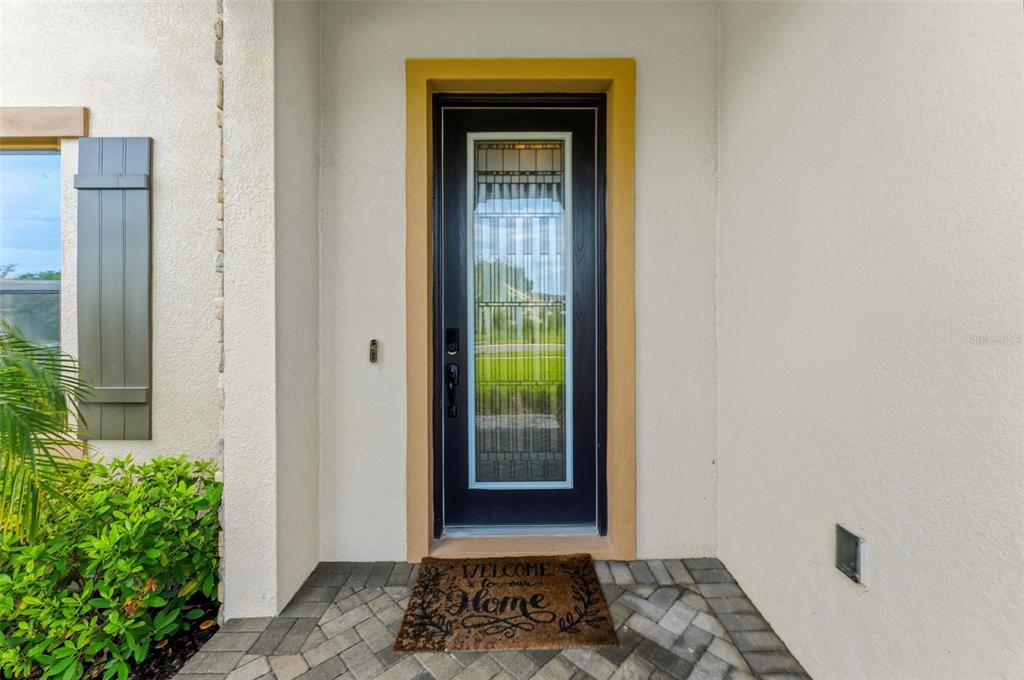 A front entryway features a black glass-paneled door with a yellow frame and a welcome mat — 10370 MEADOWRUN DRIVE, LITHIA, FL