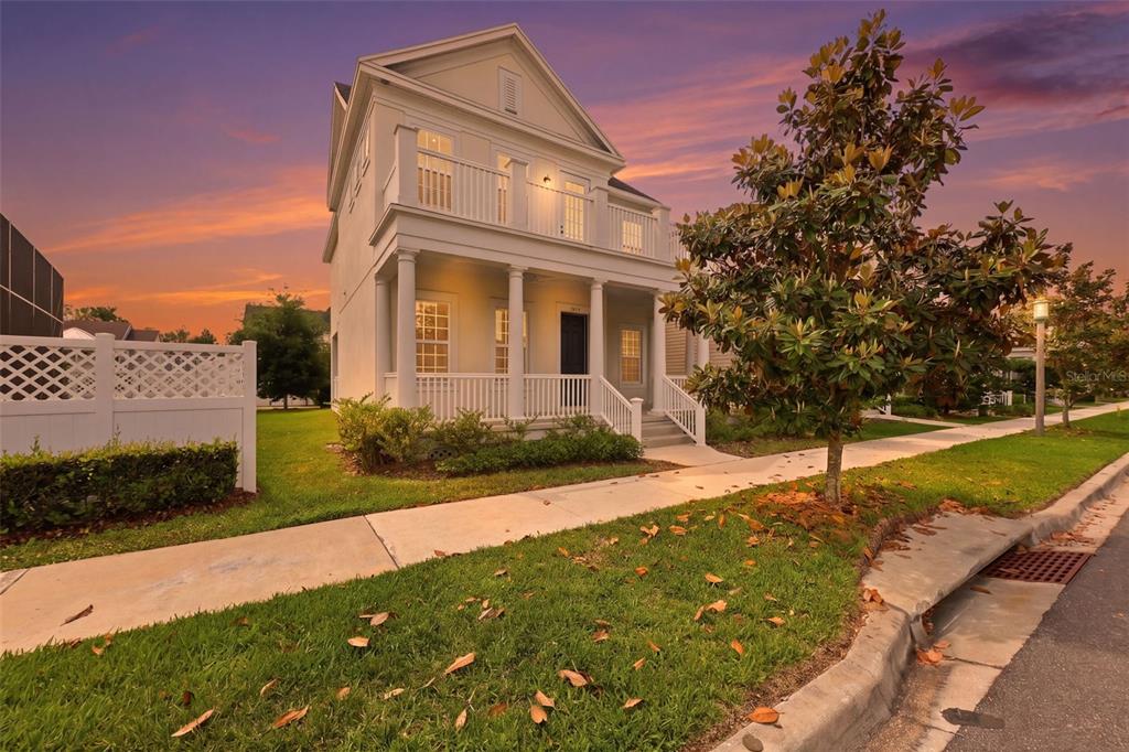 A two-story house with a front porch and balcony stands beside a sidewalk at sunset — 7410 BARRIER COVE WAY, CELEBRATION, FL