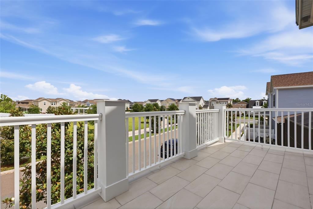A second-story balcony features white railings, light-colored tile flooring, and views of a suburban neighborhood — 7410 BARRIER COVE WAY, CELEBRATION, FL