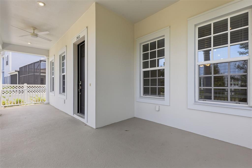 A covered porch features a dark front door, white trim, and a ceiling fan — 7410 BARRIER COVE WAY, CELEBRATION, FL