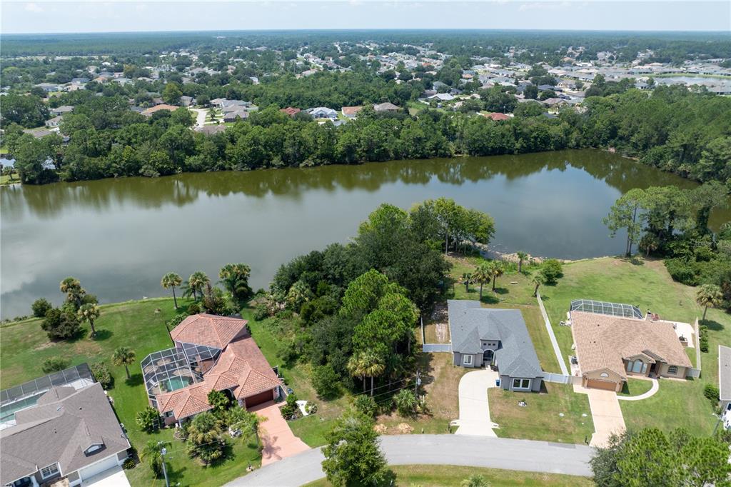 An aerial view shows three houses with pools and driveways situated along a lake — 45 LUTHER DRIVE, PALM COAST, FL