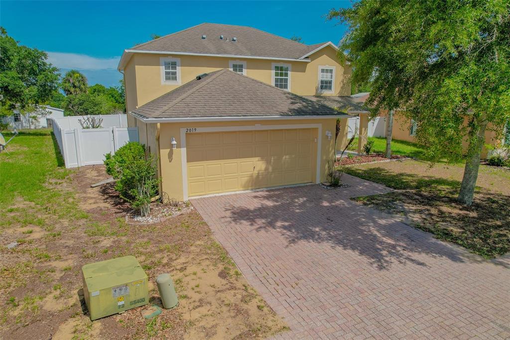 A two-story tan house with a two-car garage and a front yard with trees — 2019 HONEYBELL AVENUE, HAINES CITY, FL