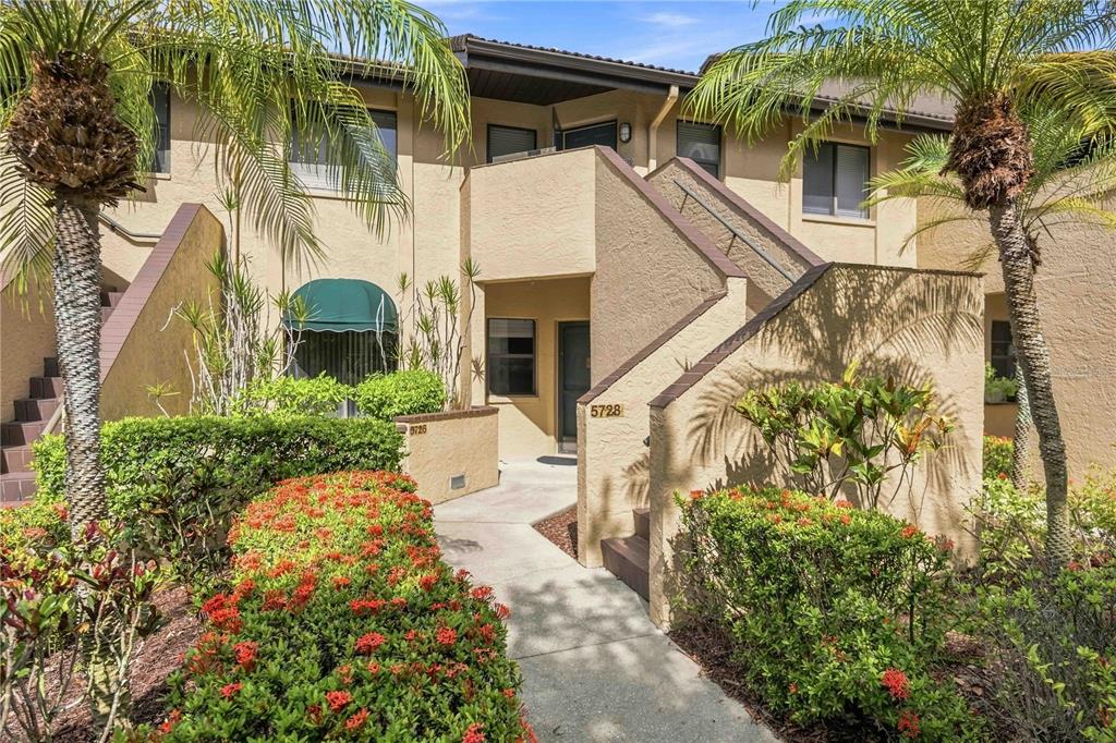 A two-story stucco apartment building features a concrete walkway, tropical landscaping, and palm trees — 5726 ASHTON LAKE DRIVE UNIT 11, SARASOTA, FL