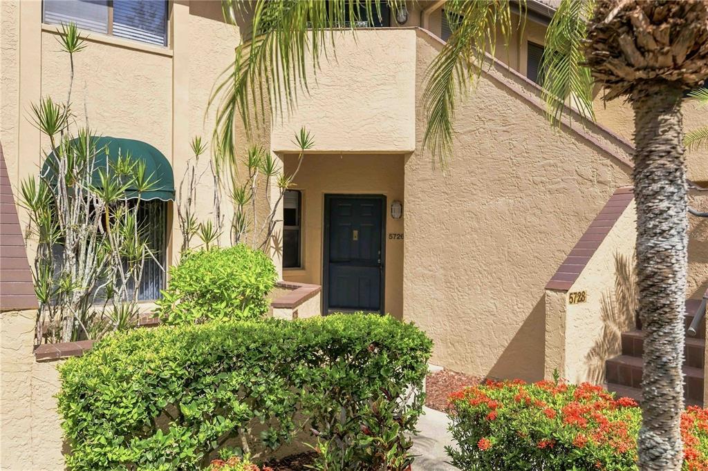 The exterior of a tan stucco residential building features a dark front door and landscaping — 5726 ASHTON LAKE DRIVE UNIT 11, SARASOTA, FL