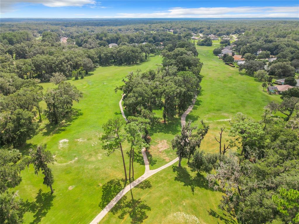 An aerial view of a grassy golf course fairway with a winding paved walking path — 19647 SW 93RD PLACE, DUNNELLON, FL