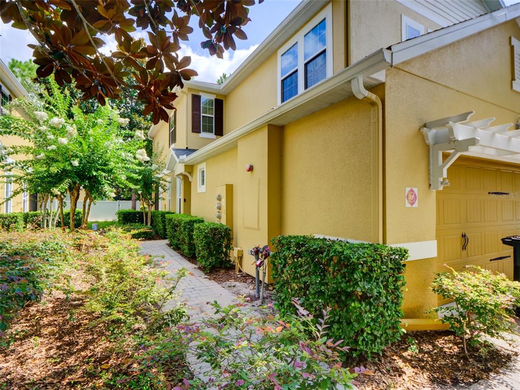 A yellow stucco townhouse exterior features a paved walkway, manicured hedges, and a garage — 8218 MYSTIC VIEW WAY UNIT 2801, WINDERMERE, FL