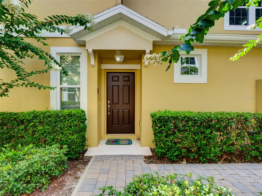 The exterior of a yellow house features a dark brown front door and a paved walkway — 8218 MYSTIC VIEW WAY UNIT 2801, WINDERMERE, FL