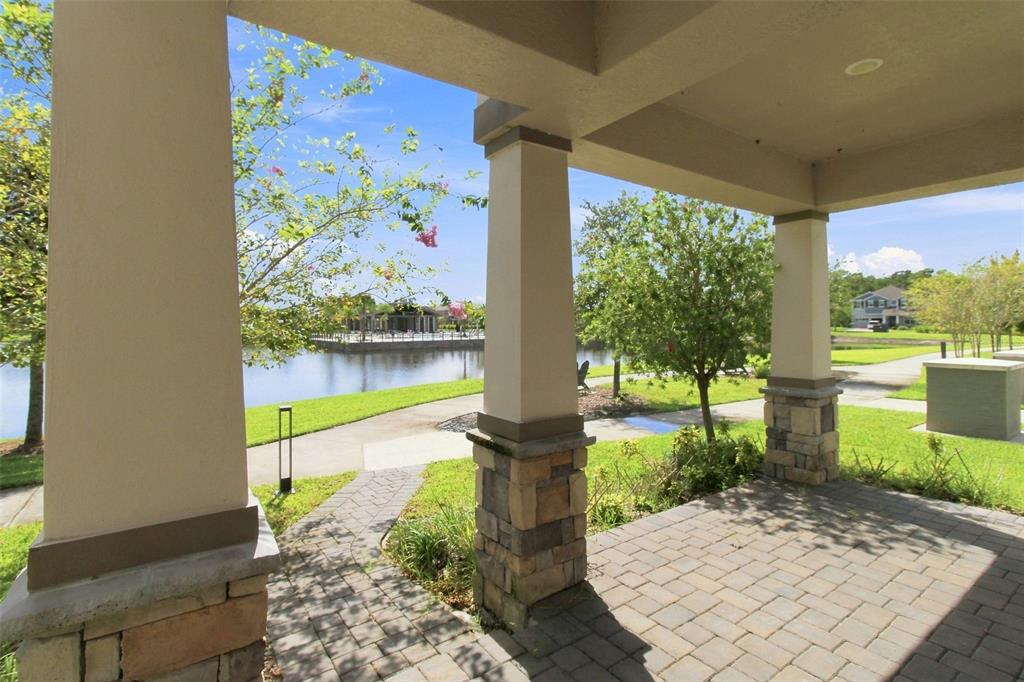 A covered stone-paved patio overlooks a lake with a walking path and a small dock — 761 FIREROCK LANE, DEBARY, FL