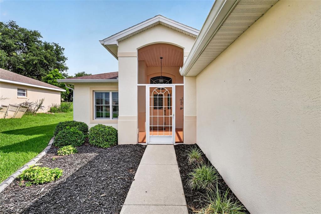 A concrete walkway leads to the screened front entryway of a beige stucco house — 5809 BOUNTY CIRCLE, TAVARES, FL
