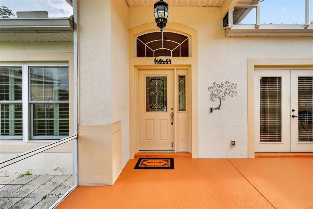 A front entryway features a tan door with a sidelight, a welcome mat, and orange flooring — 5809 BOUNTY CIRCLE, TAVARES, FL
