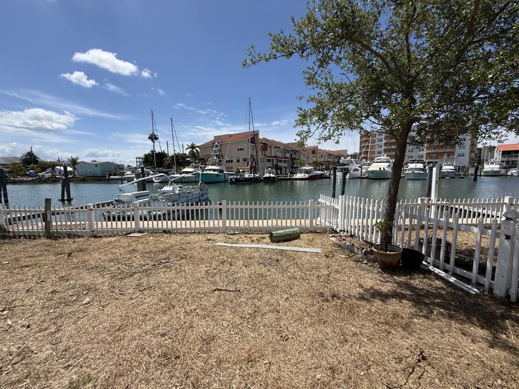 A view of a grassy yard with a white fence overlooking a marina with boats — 249 BOCA CIEGA DRIVE, MADEIRA BEACH, FL