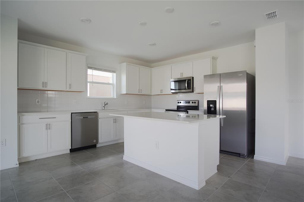 A modern kitchen features white cabinets, stainless steel appliances, a center island, and gray tile flooring — 437 WATERFORD DRIVE, LAKE ALFRED, FL
