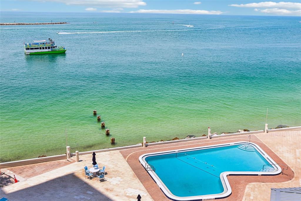 An elevated view of a swimming pool overlooking the ocean with a boat nearby — 450 S GULFVIEW BOULEVARD UNIT 605, CLEARWATER BEACH, FL