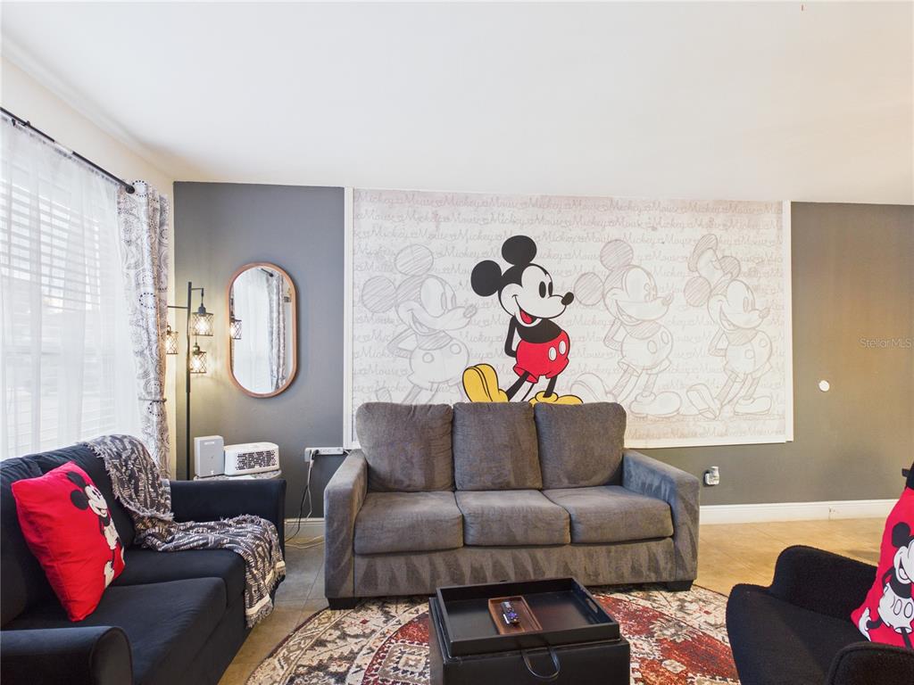 A living room features a grey sofa against a wall with a large Mickey Mouse mural — 3100 PARKWAY BOULEVARD UNIT 728, KISSIMMEE, FL