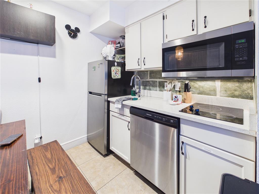 A small kitchen features white cabinets, stainless steel appliances, and a stone-tiled backsplash — 3100 PARKWAY BOULEVARD UNIT 728, KISSIMMEE, FL