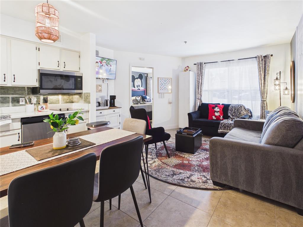 An open-concept living room and kitchen area features tile flooring, a dining table, and sofas — 3100 PARKWAY BOULEVARD UNIT 728, KISSIMMEE, FL