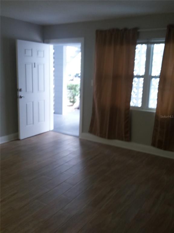A room with wood-look tile flooring, a white entry door, and a window with curtains — 1710 S WASHINGTON AVENUE UNIT 01, TITUSVILLE, FL
