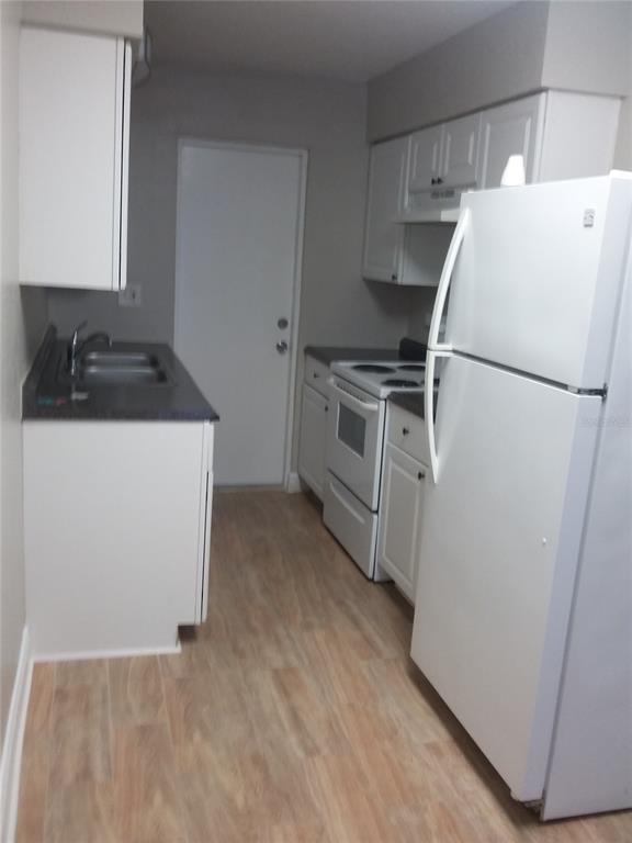 A kitchen features white cabinets, a black countertop, a white stove, and a white refrigerator — 1710 S WASHINGTON AVENUE UNIT 01, TITUSVILLE, FL