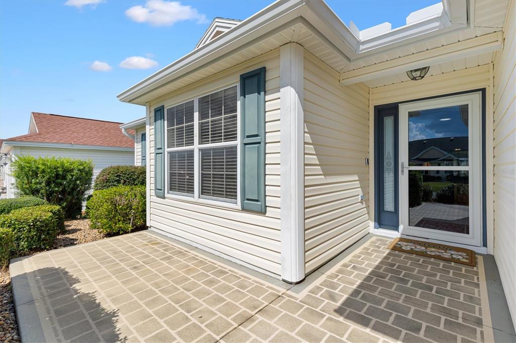 A beige vinyl-sided house exterior features a front patio, a window with shutters, and a door — 2494 FLINTSHIRE AVENUE, THE VILLAGES, FL