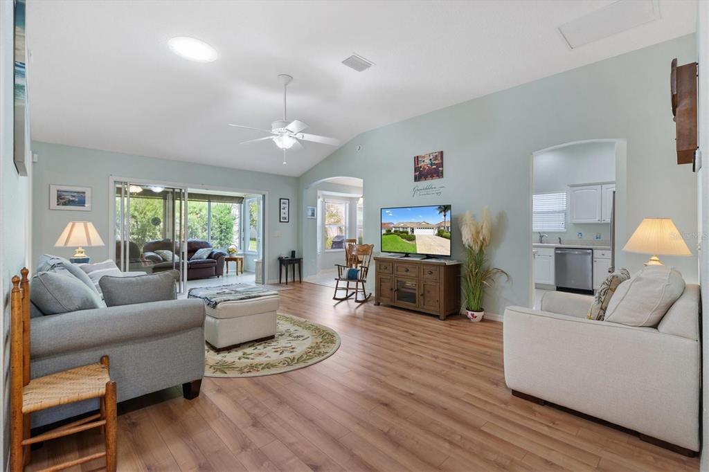 A living room with light blue walls, wood-look flooring, a ceiling fan, and a television — 2494 FLINTSHIRE AVENUE, THE VILLAGES, FL