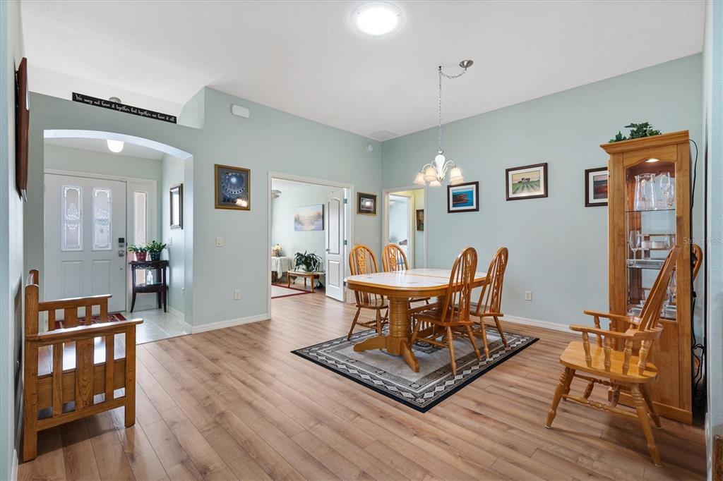 A dining room with light blue walls, wood flooring, a wooden table, and a display cabinet — 2494 FLINTSHIRE AVENUE, THE VILLAGES, FL