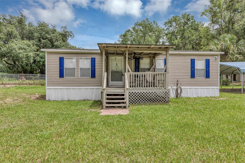 A tan mobile home with blue shutters and a covered front porch sits on grass — 2756 NE 34TH ROAD, COLEMAN, FL
