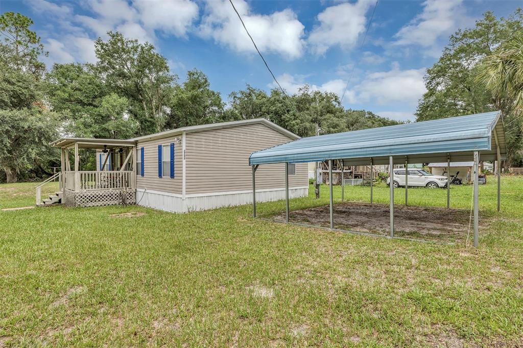 A tan mobile home with a wooden porch and a detached metal carport on grass — 2756 NE 34TH ROAD, COLEMAN, FL