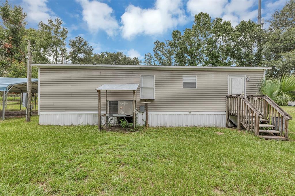 The exterior of a single-wide mobile home features beige siding, a window unit, and wooden stairs — 2756 NE 34TH ROAD, COLEMAN, FL