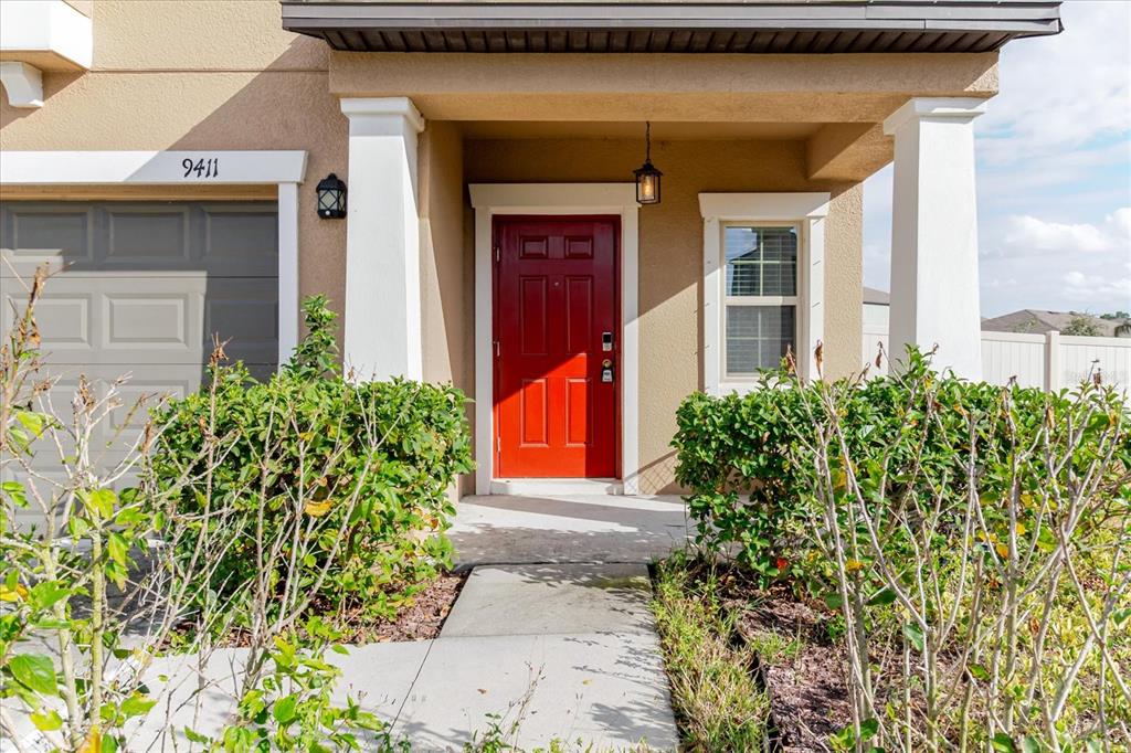 A red front door is centered under a covered porch next to a garage — 9411 LEMON DROP LOOP, SUN CITY CENTER, FL