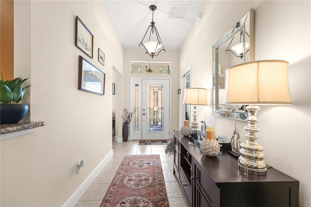 A tiled entryway features a dark console table, a decorative runner, and a glass-paneled front door — 571 TROY LOOP, THE VILLAGES, FL