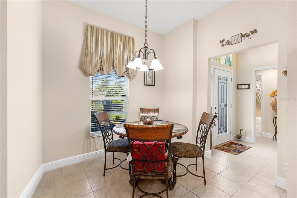 A dining area features a round table with four chairs, a chandelier, and tile flooring — 571 TROY LOOP, THE VILLAGES, FL