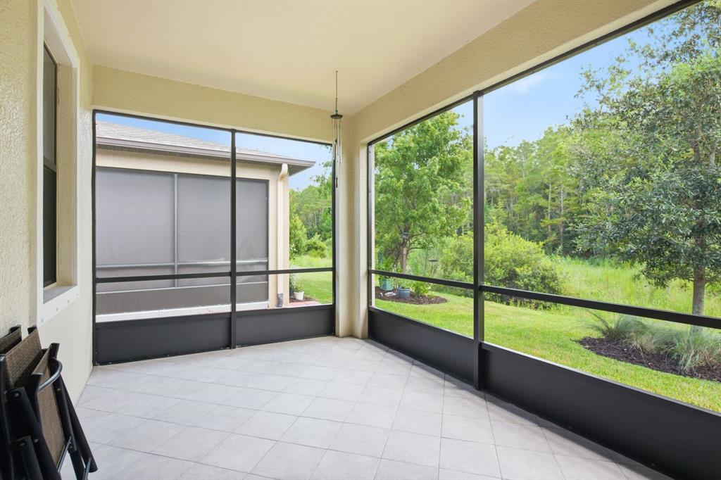 A screened-in patio with light tile flooring overlooks a grassy yard and wooded area — 16936 BALANCE COVE, LAND O LAKES, FL