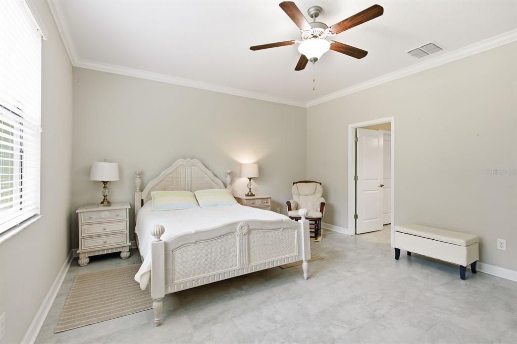 A bedroom features a white bed frame, two nightstands, a rocking chair, and tile flooring — 16936 BALANCE COVE, LAND O LAKES, FL
