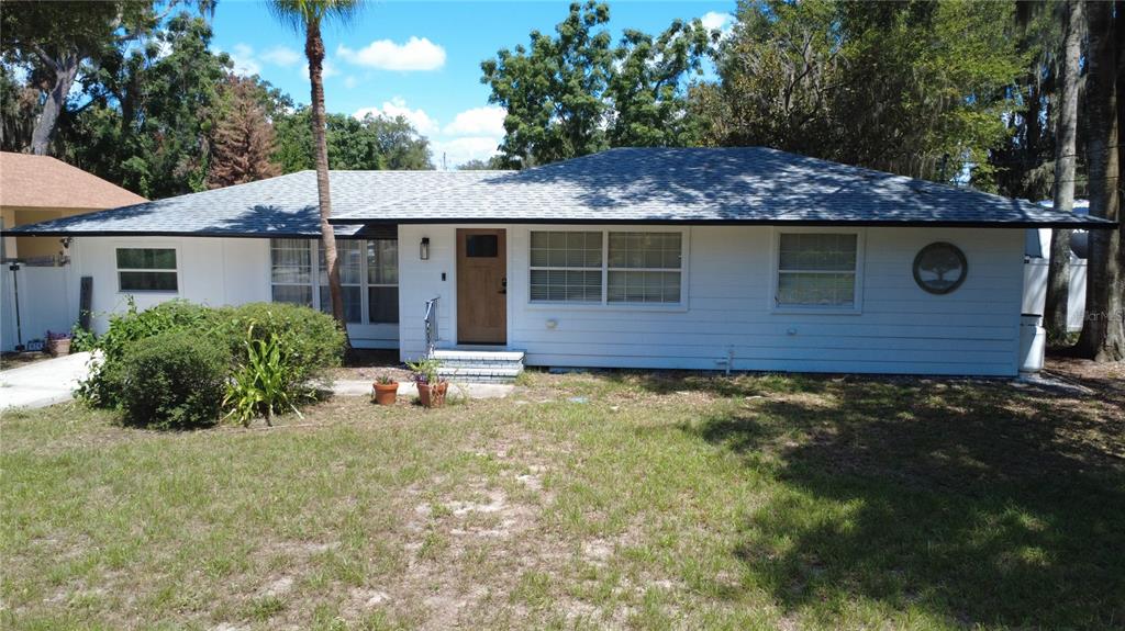 A single-story white house with a wooden front door and a gray shingled roof — 925 E 10TH AVENUE, MOUNT DORA, FL