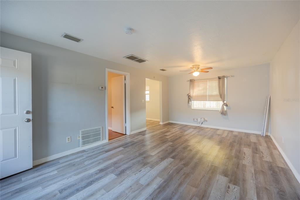 An empty living room features light gray walls, wood-look flooring, a ceiling fan, and windows — 400 S METEOR AVENUE, CLEARWATER, FL
