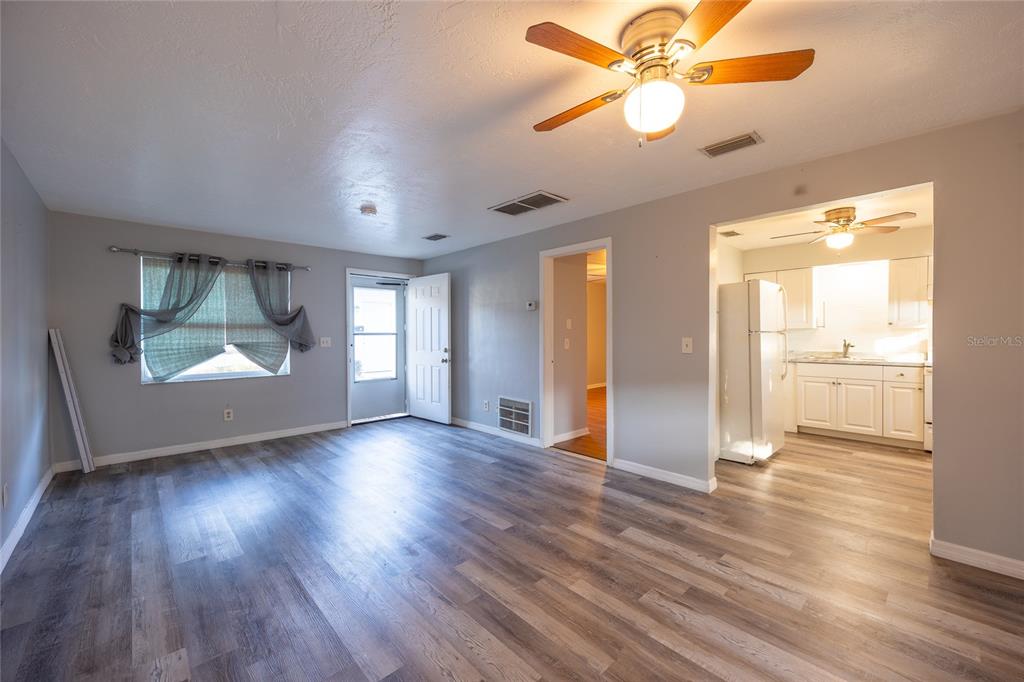 A living room with gray wood-look flooring, a ceiling fan, and an adjacent kitchen — 400 S METEOR AVENUE, CLEARWATER, FL
