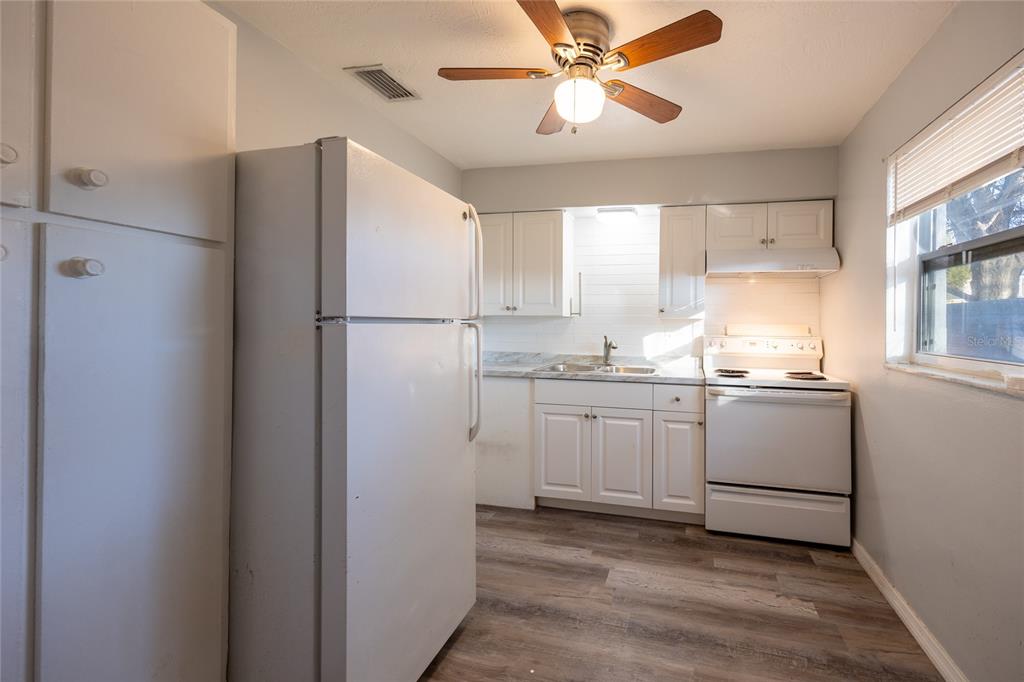 A kitchen features white cabinets, a white refrigerator, a white stove, and wood-look flooring — 400 S METEOR AVENUE, CLEARWATER, FL