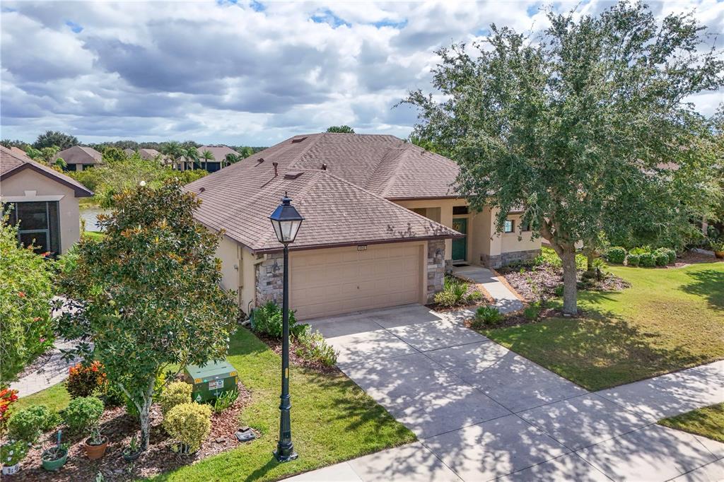 An aerial view of a single-story house with a tan garage and a large tree — 8860 BRIDGEPORT BAY CIRCLE, MOUNT DORA, FL