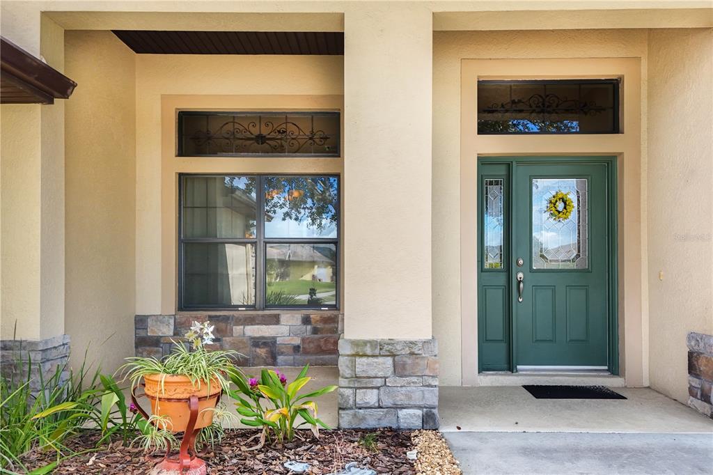 The exterior entrance features a green front door, a large window, and stone base accents — 8860 BRIDGEPORT BAY CIRCLE, MOUNT DORA, FL