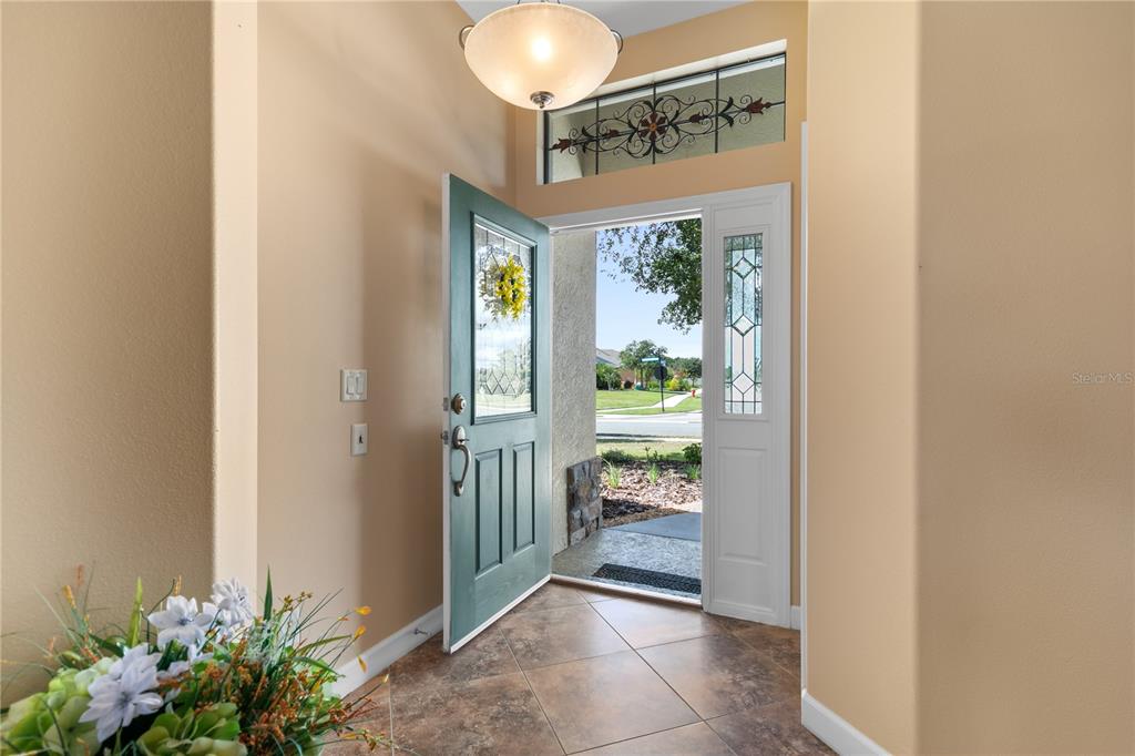 An open front door reveals a tiled entryway with a decorative transom window above — 8860 BRIDGEPORT BAY CIRCLE, MOUNT DORA, FL