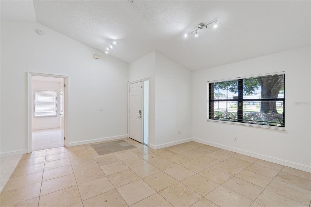 A bright room with white walls, tile flooring, a vaulted ceiling, and a large window — 9433 PALM TREE DRIVE, WINDERMERE, FL